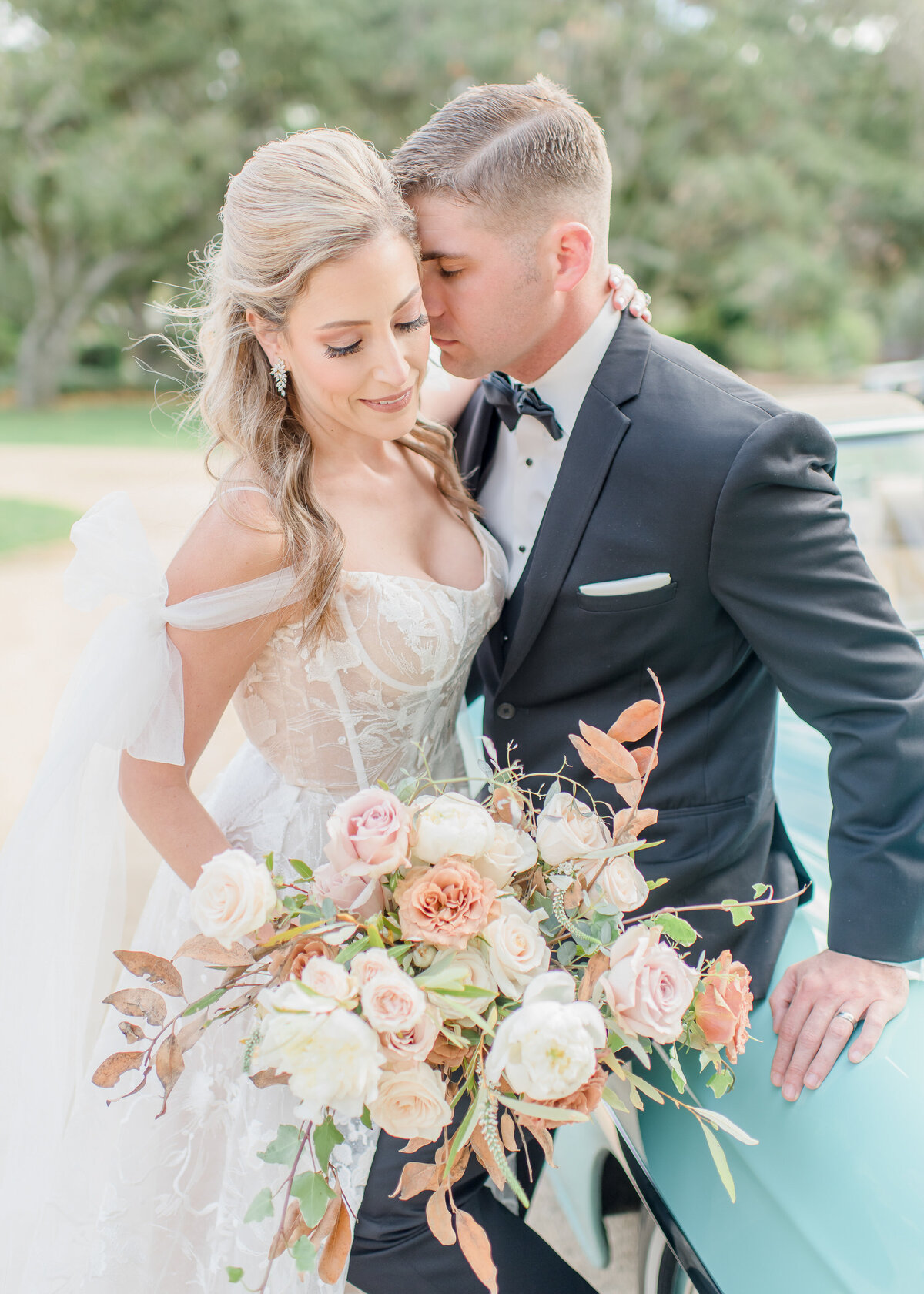wedding couple holding flowers in front of blue car at garden wedding