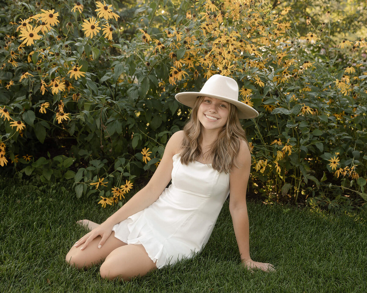 Senior girl sitting in front of a patch of yellow flowers.