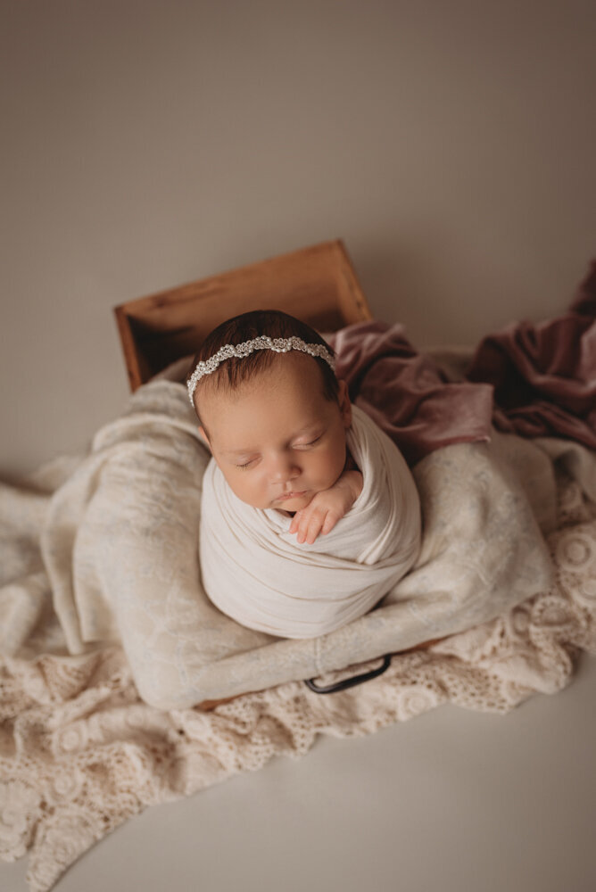 Newborn photo shoot photographed by Atlanta, Georgia newborn photographer with baby posing on neutral fabric with dainty headband on and sleeping.