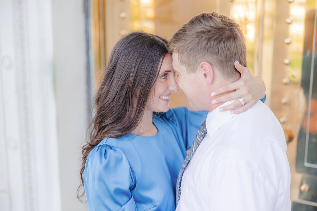 A woman in a blue dress holds the neck of her fiancee while touching foreheads in a doorway