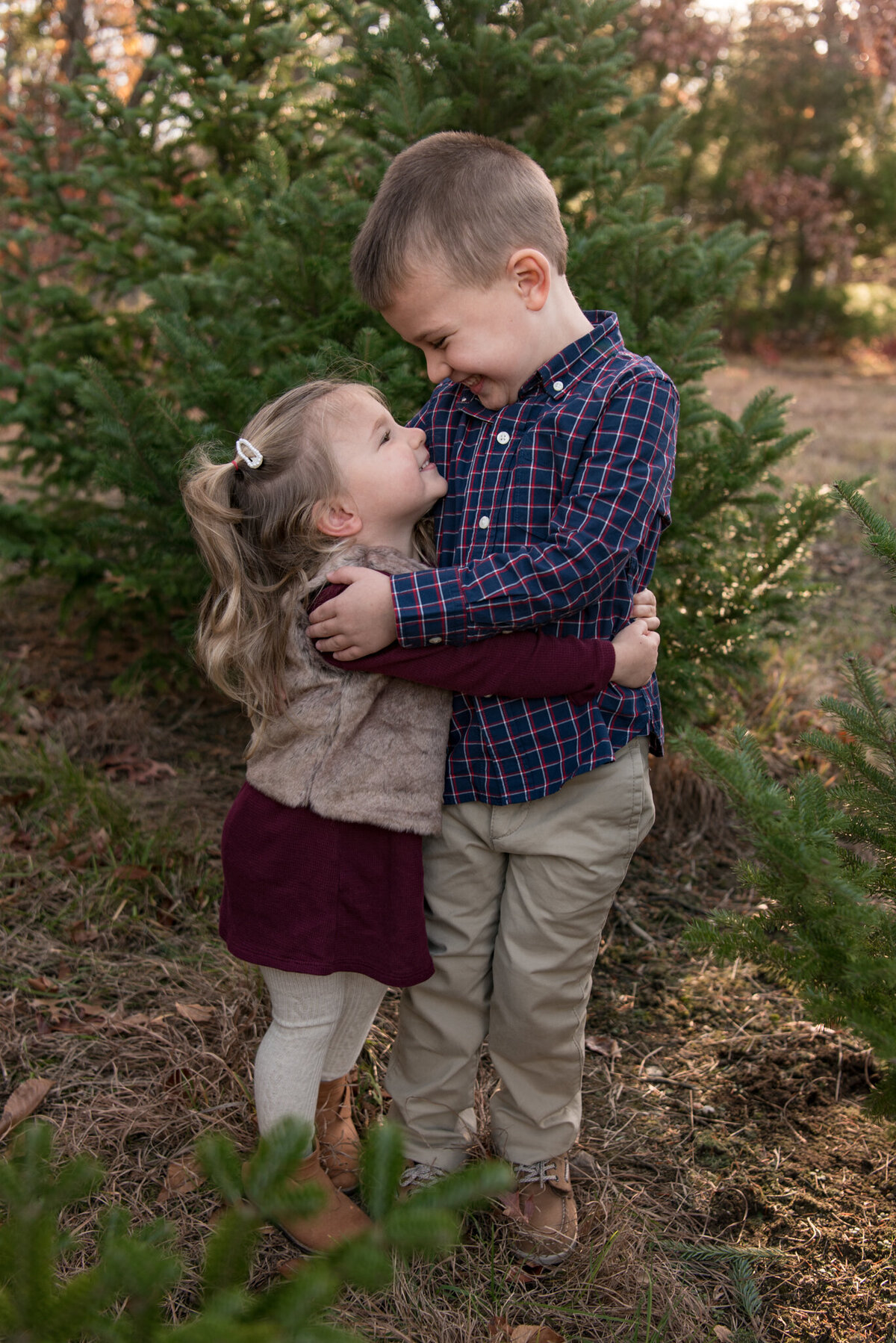 Brother and sister hugging and smiling at each other at Christmas Tree Farm