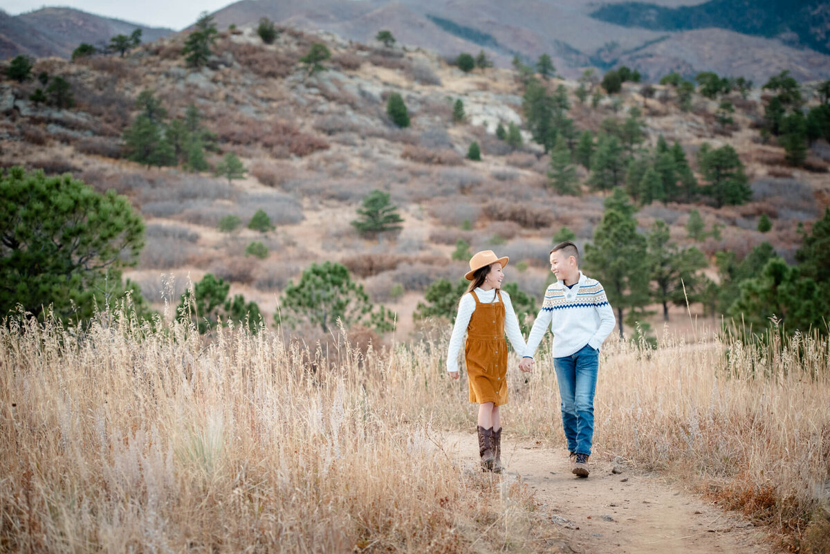 A brother and sister hold hands while walking on a mountain trail