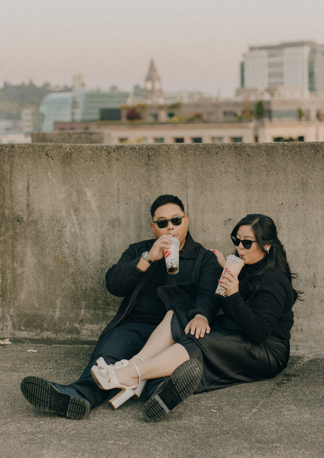 Couple dressed in all black with sunglasses sipping on boba