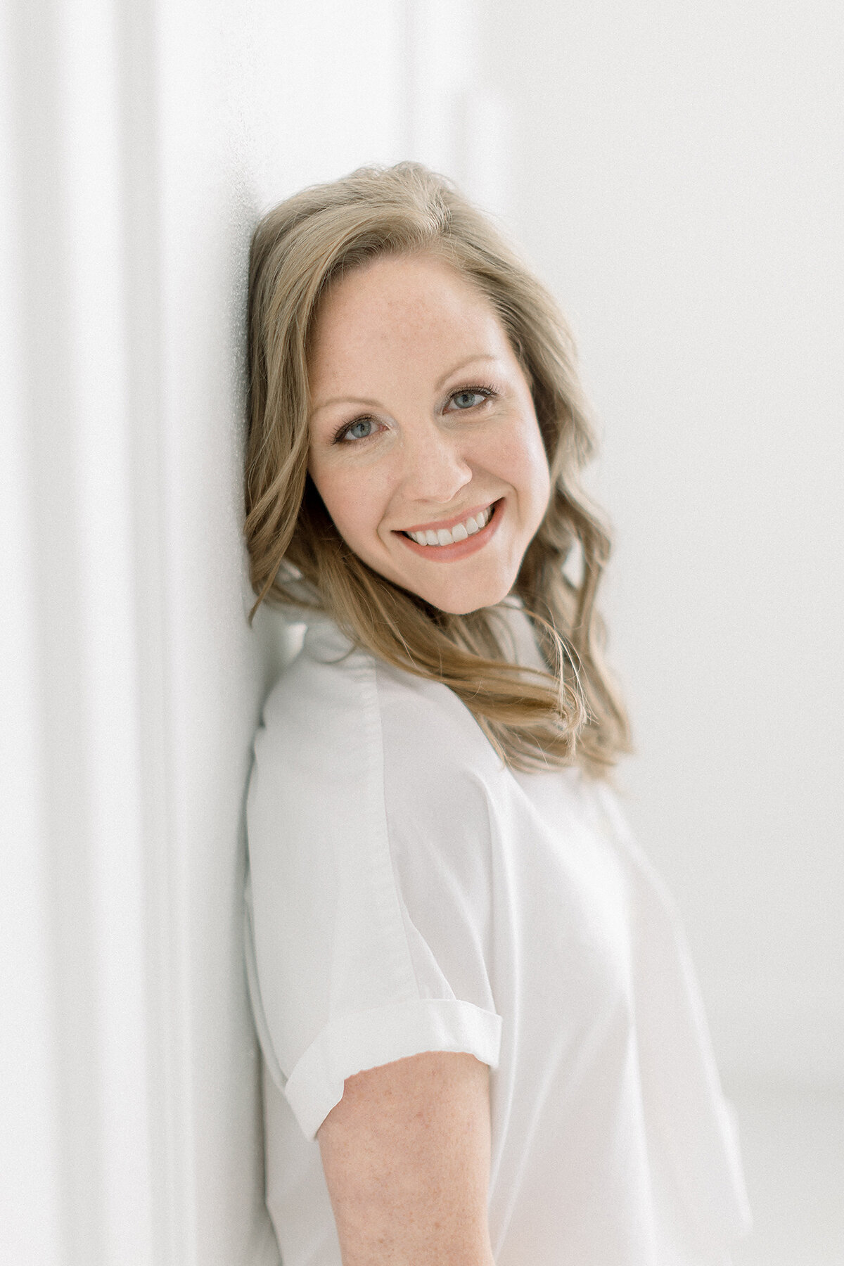 Close up professional headshot photo of a DFW business woman looking at the camera and smiling as she poses in a photography studio.