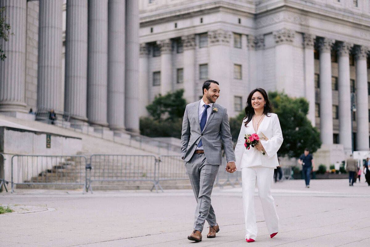 The bride and groom are happily walking outside New York City Hall. Image by Jenny Fu Studio