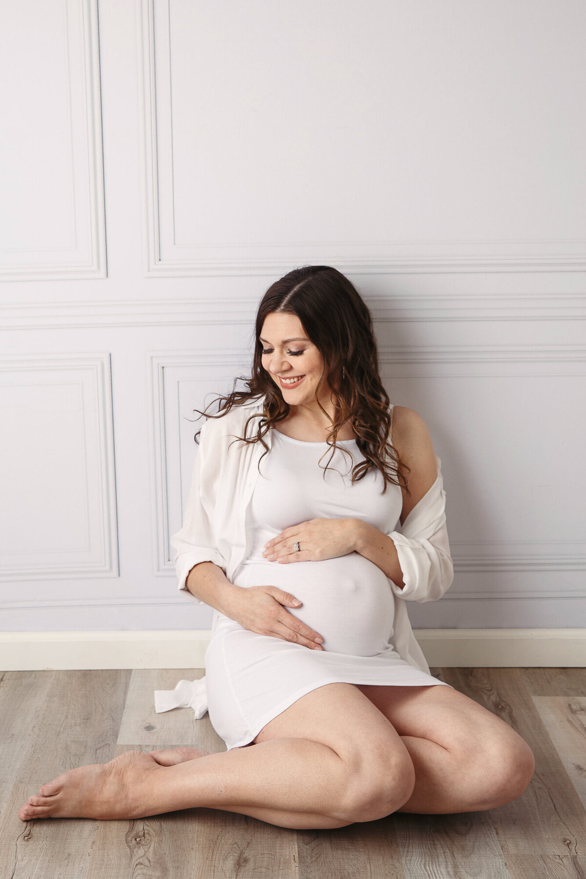 Young pregnant mom to be sitting against a wall and holding her tummy