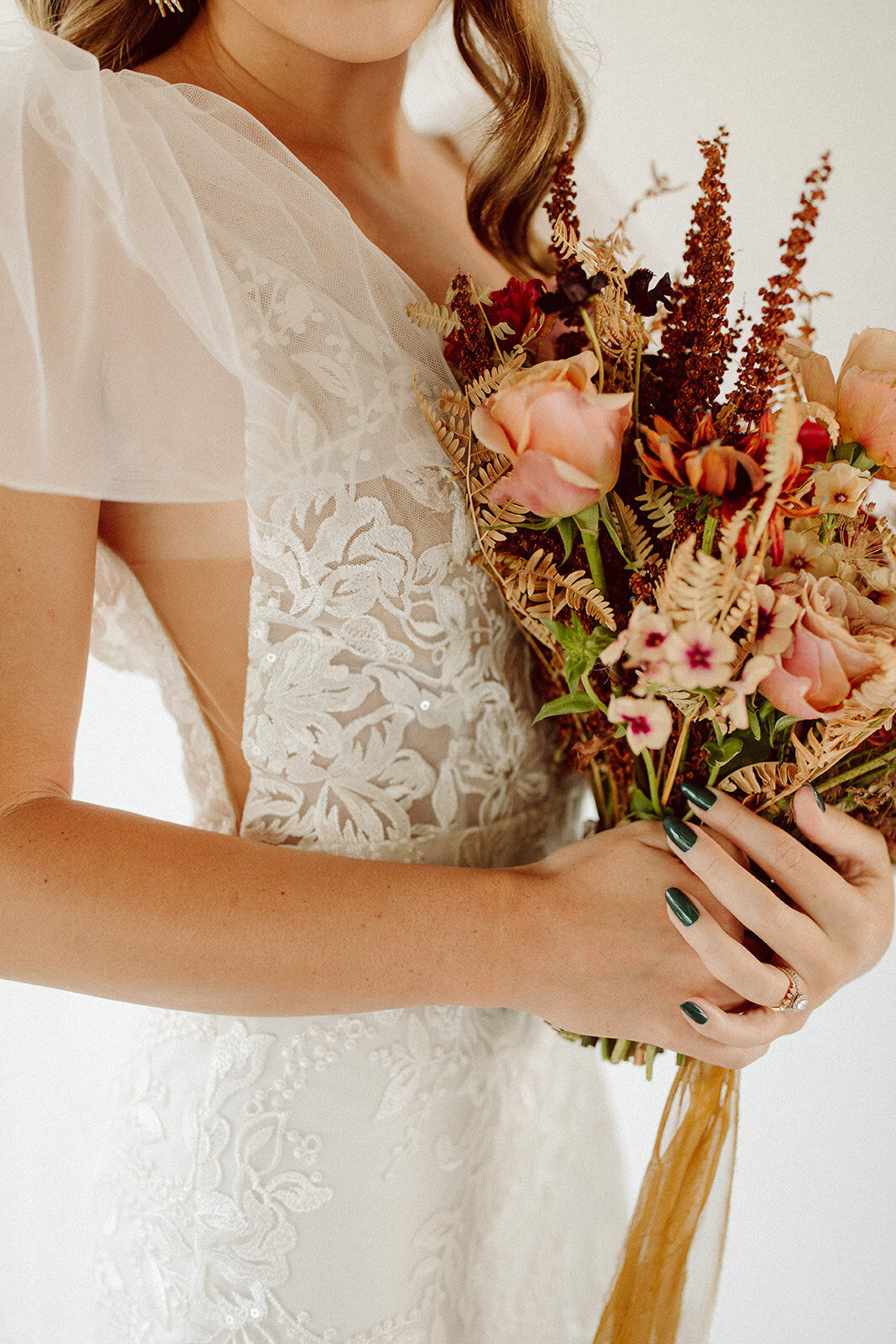 Close-up shot of bride wearing a white lace wedding gown holding a bouquet of blush and cream flowers.