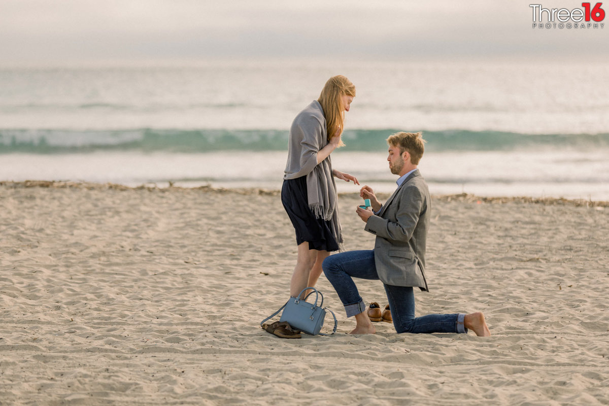 Man gets down on knee on the sand at Newport Beach and proposes marriage to his girlfriend