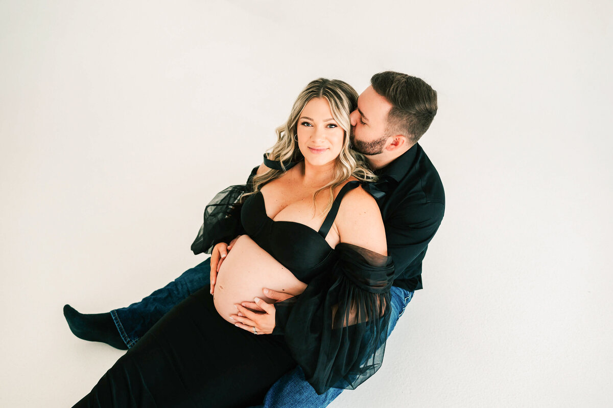 pregnant couple sitting on the floor cuddling in Springfield Mo maternity photography studio