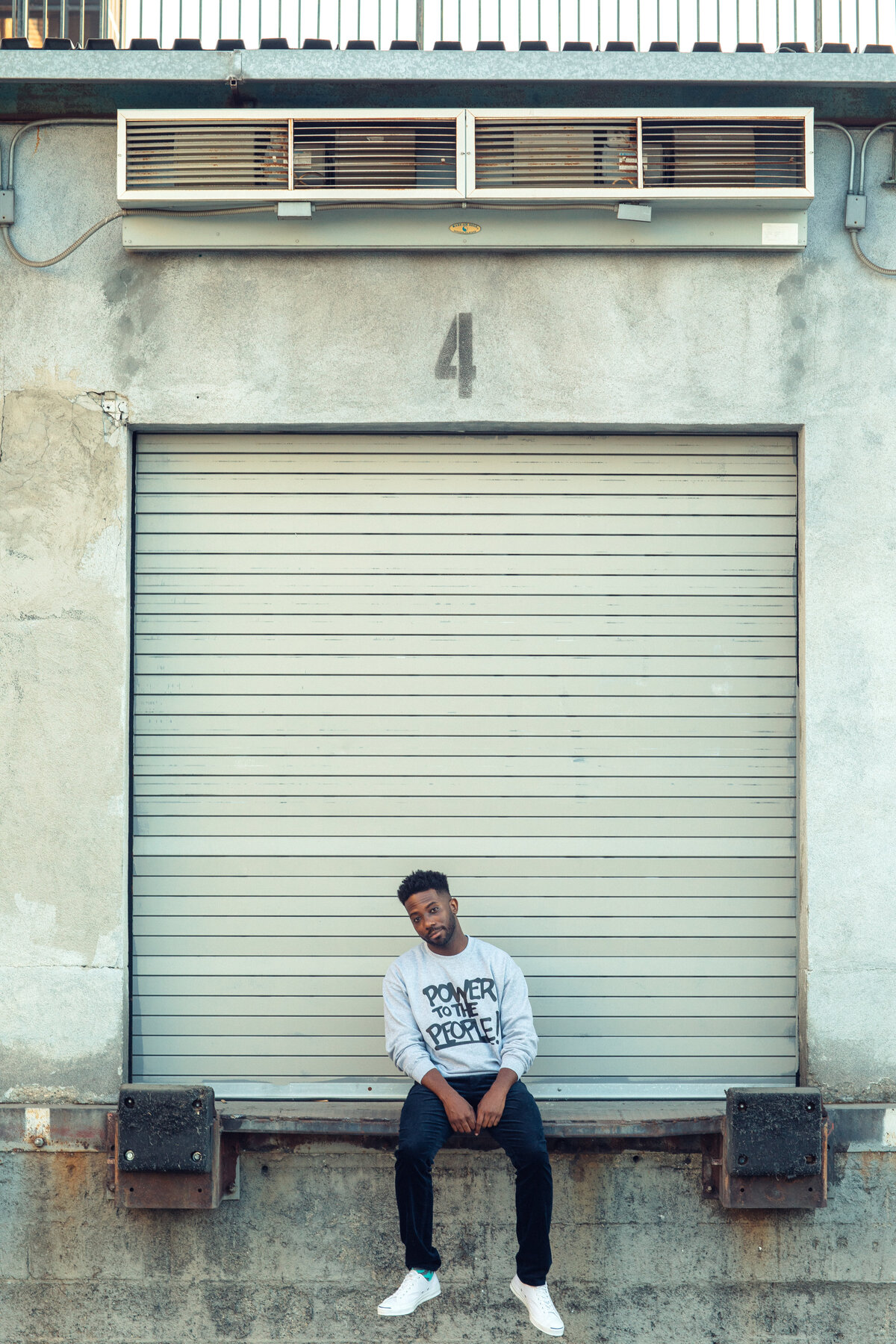 Portrait Photo Of Young Black Man Gray Sweater Leaning Against a Pull Down Gate Los Angeles