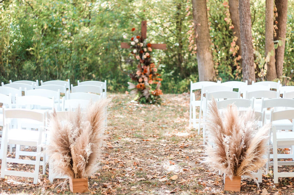 Outdoor wedding ceremony setup with pampas grass and floral-decorated cross
