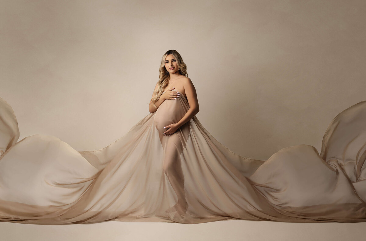 A pregnant woman stands in a studio covering with a long flowing sheet taken by a New Orleans Maternity Photographer