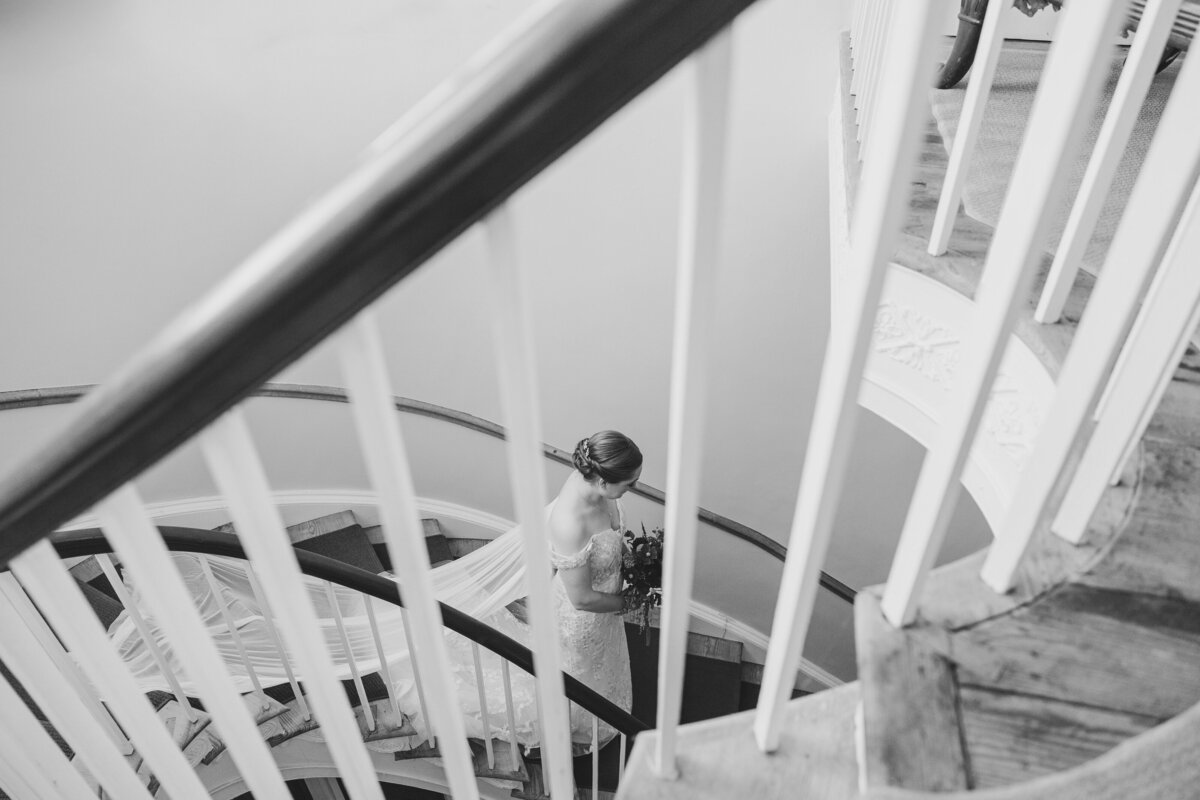 View from in between a staircase railing of a person in a wedding dress walking down the stairs 