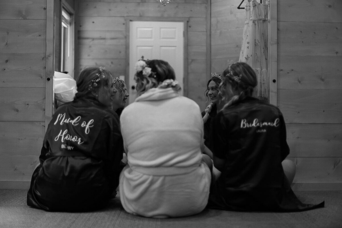 Bridesmaids sitting with “Maid of Honor” and “Bridesmaid” robes, facing away
