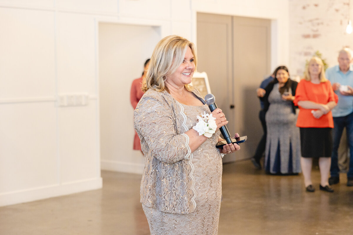 The mother of the bride stands with a microphone, delivering an emotional speech to wedding guests.