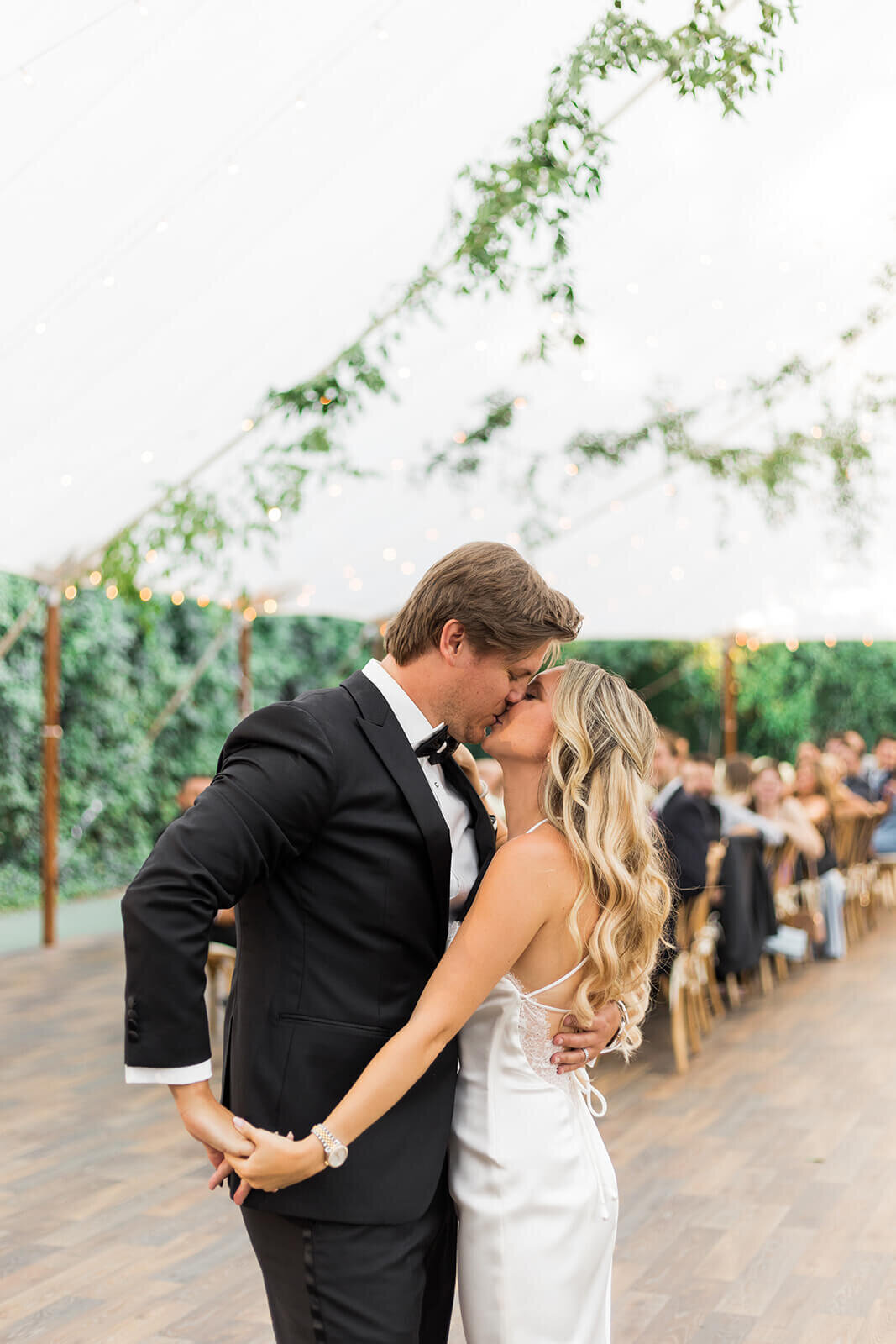 Bride and groom kissing under canopy with greenery