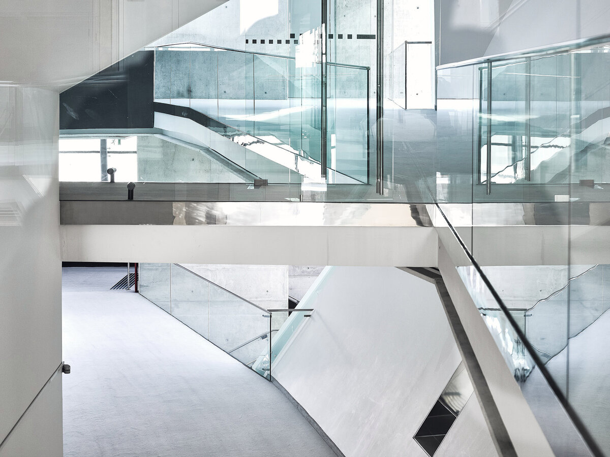 Minimalistisches Treppenhaus mit Glasbrüstungen und Sichtbeton – moderne Architektur in klarer Linienführung, aufgenommen von Architekturfotograf Atelier Schulte in Wien.