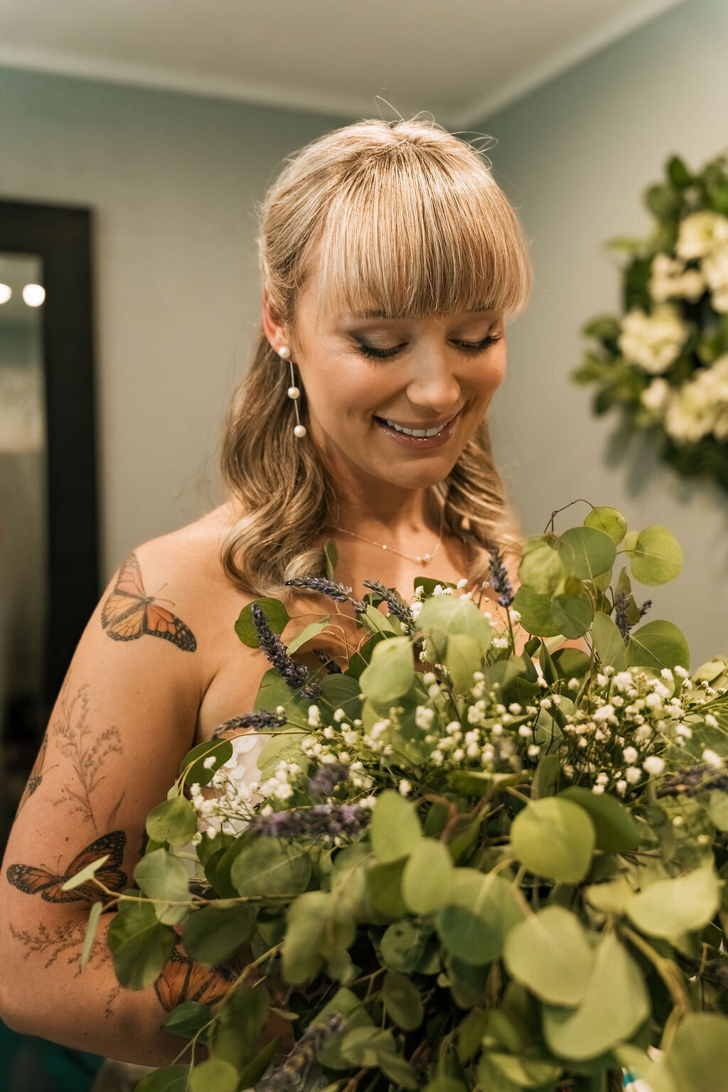 A bride smiles while holding a bouquet of flowers, representing bridal makeup done by Looks with Libby.