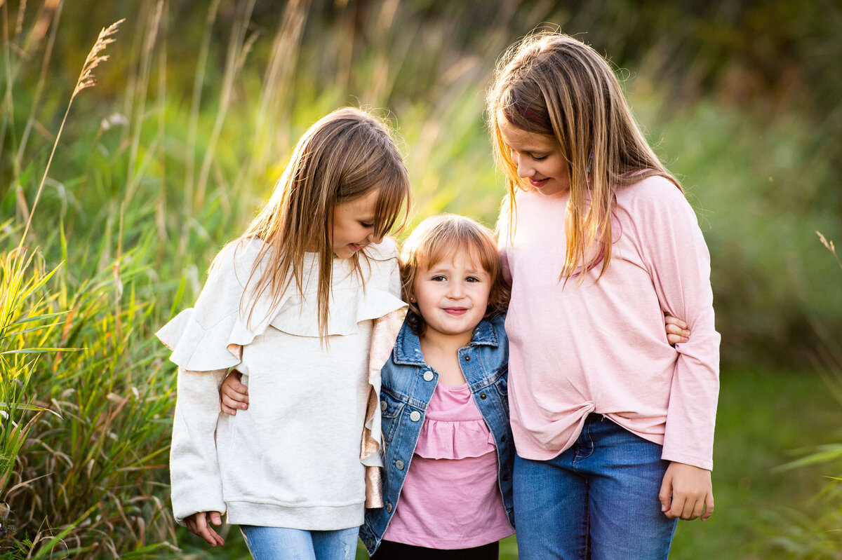 family photos in Ottawa of three sisters hugging in a field at sunset golden hour