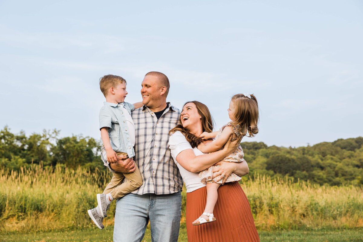 A Pittsburgh family photographer captures a moment of laughter in a field with the parents holding up their children.