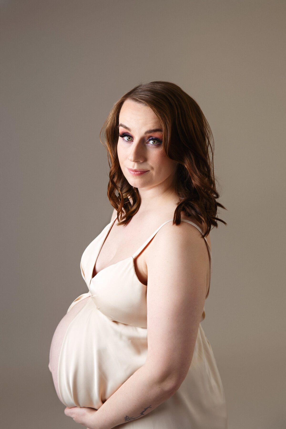 Close up portrait of a  pregnant woman wearing a gold gown photographed on a brown background