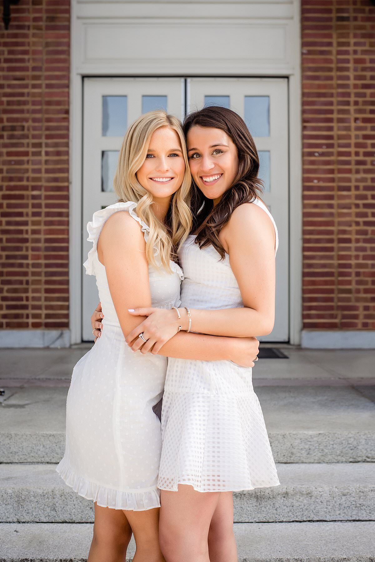 Roommates wearing white dresses and hugging one another on the steps of historic Vanderbilt campus building