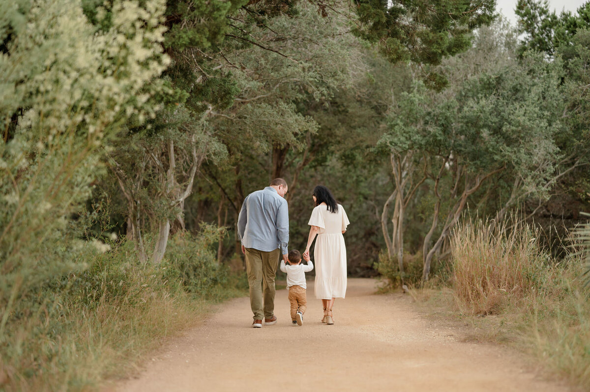 Family of three walk down a path at Hardberger Park in San Antonio during family pictures.