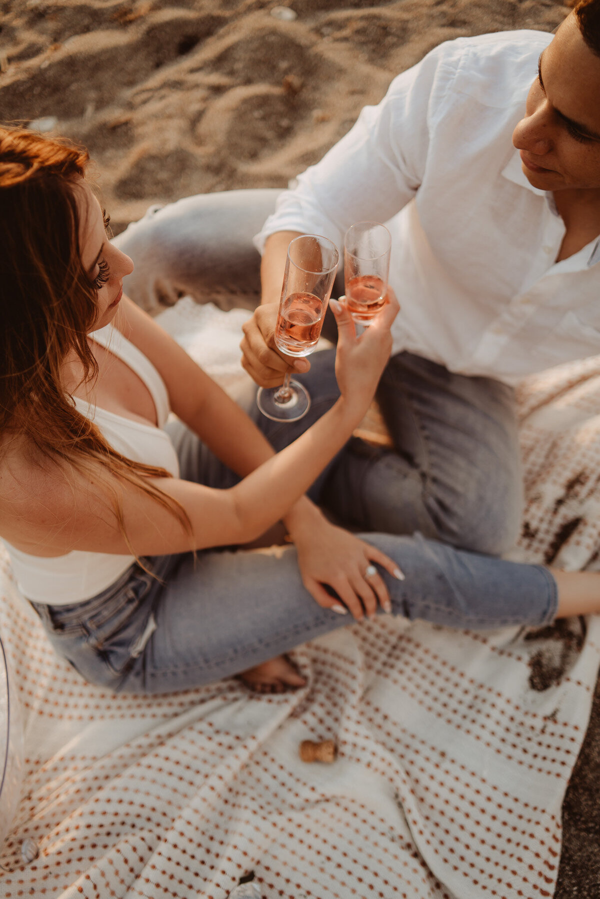 a couple celebrating their engagement sitting on the beach celebrating with cheers, champagne