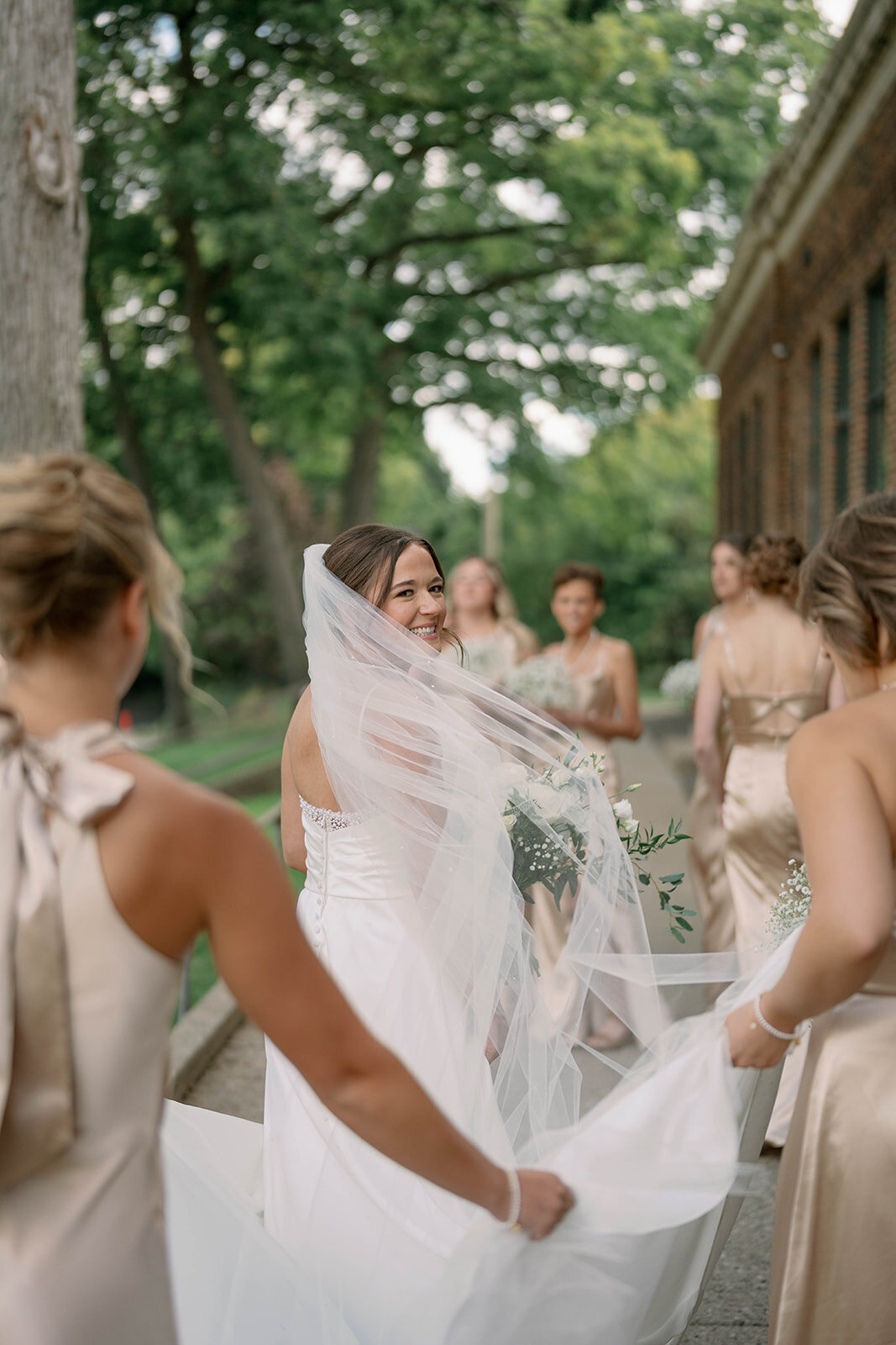 Bride surrounded by bridesmaids in champagne bridesmaid dresses as they walk together during a September wedding at Leona Road.
