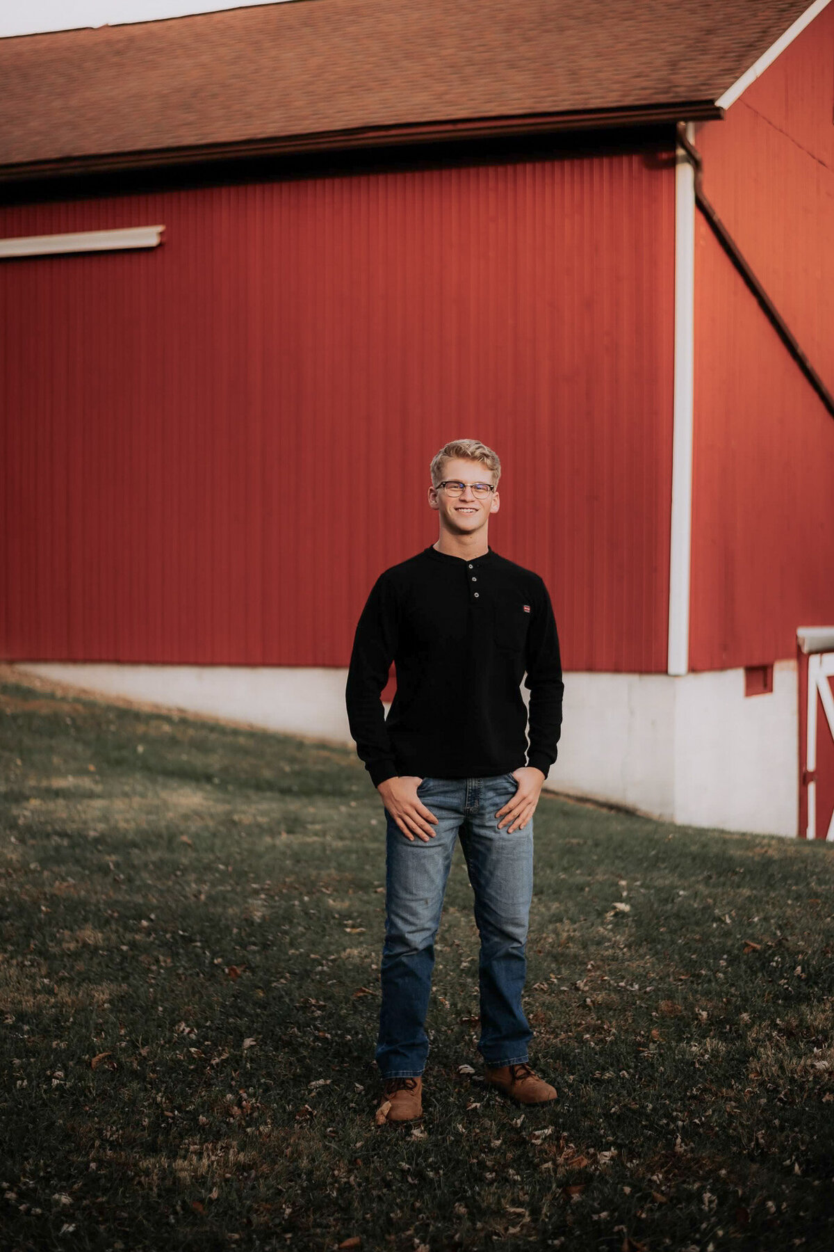 A male high school senior poses confidently in front of a rustic red barn in Cuyahoga Valley National Park, capturing the essence of a classic, outdoor portrait. Surrounded by the park's natural beauty, this image reflects the senior's individuality and style, making it a perfect choice for students looking for timeless, nature-inspired senior photos in Northeast Ohio.