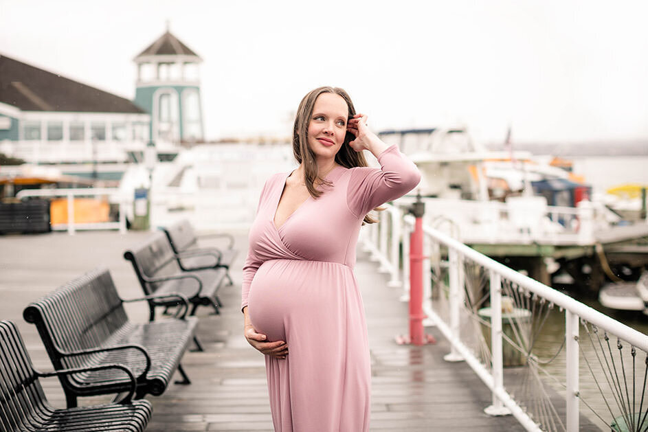 Woman in pink dress holding pregnant belly on the dock in Old Town Alexandria