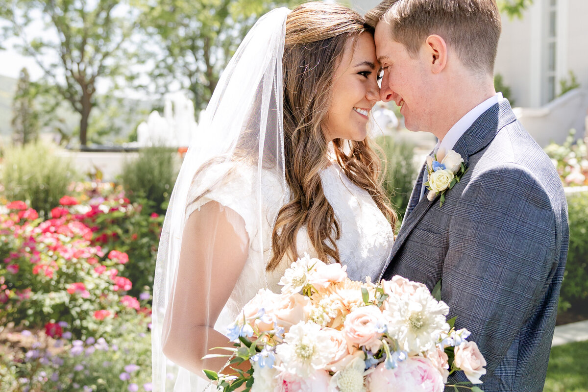 The bride and groom lean close with foreheads touching, sharing a heartfelt moment amidst colorful temple gardens.