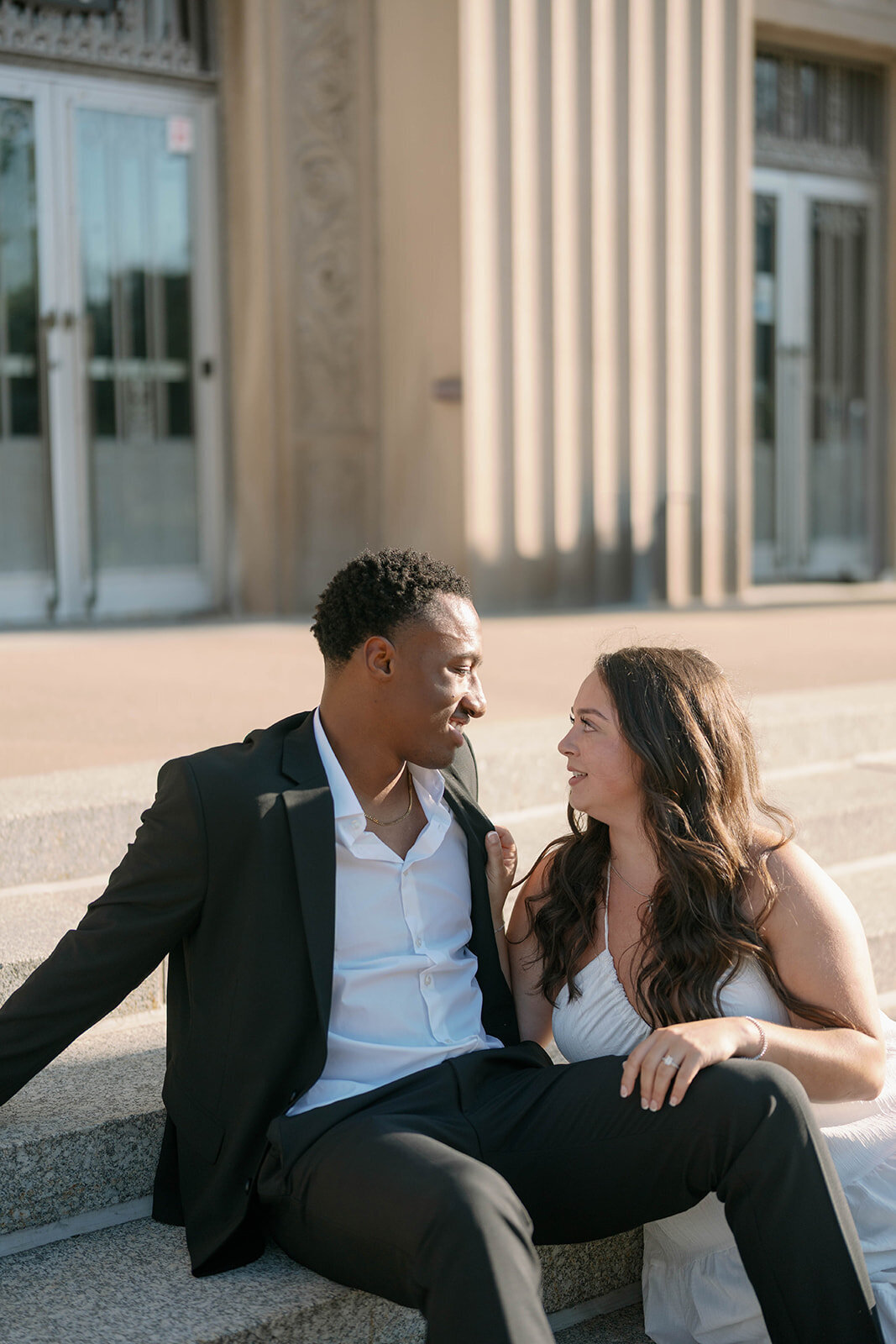 Romantic Kalamazoo engagement photo of couple sitting on steps at golden hour smiling together.