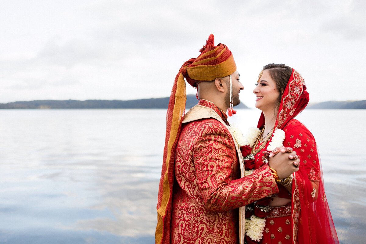 Bride and groom with Hindu ceremony attire holding hands with the water in the back