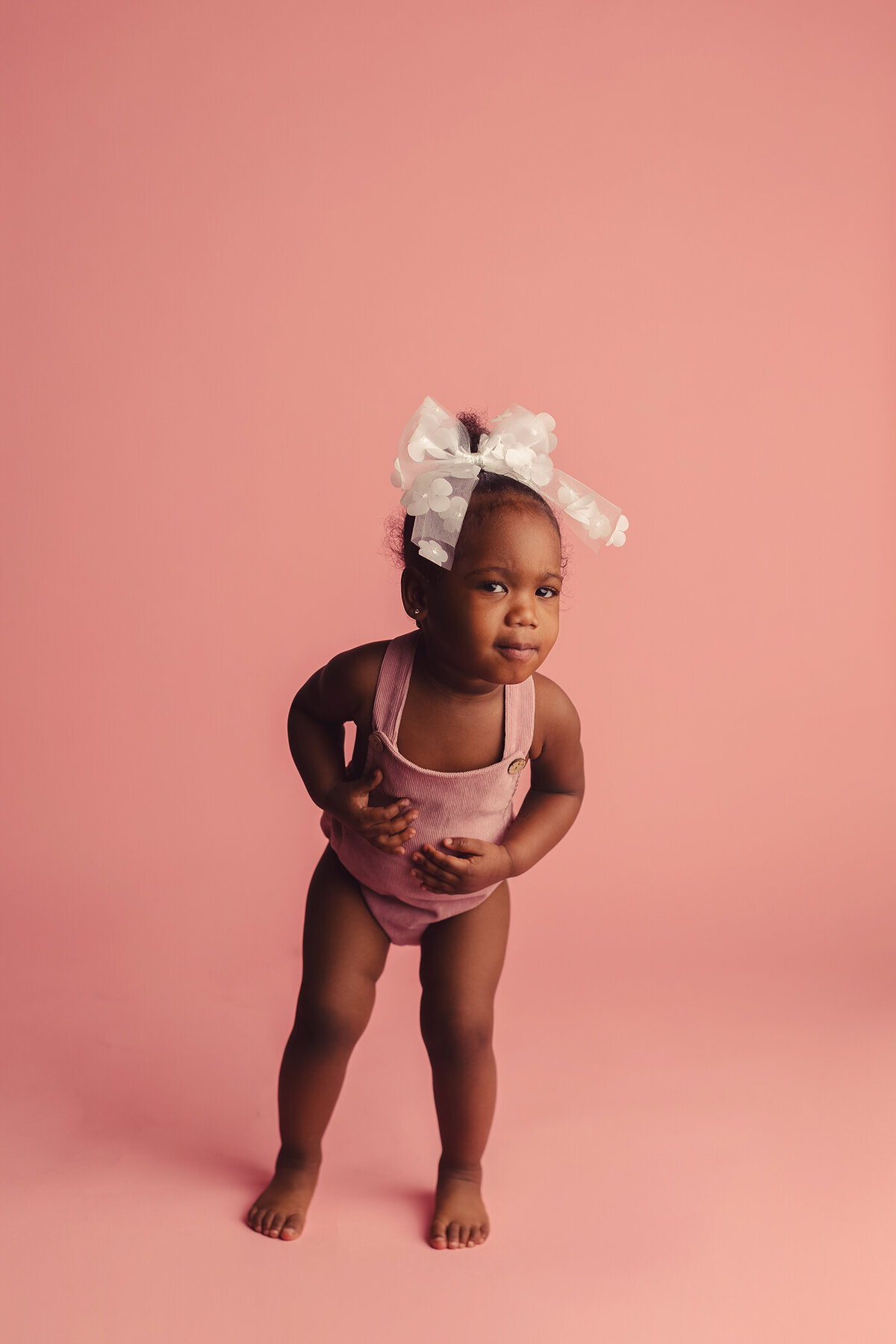 little girl in pink romper on pink backdrop