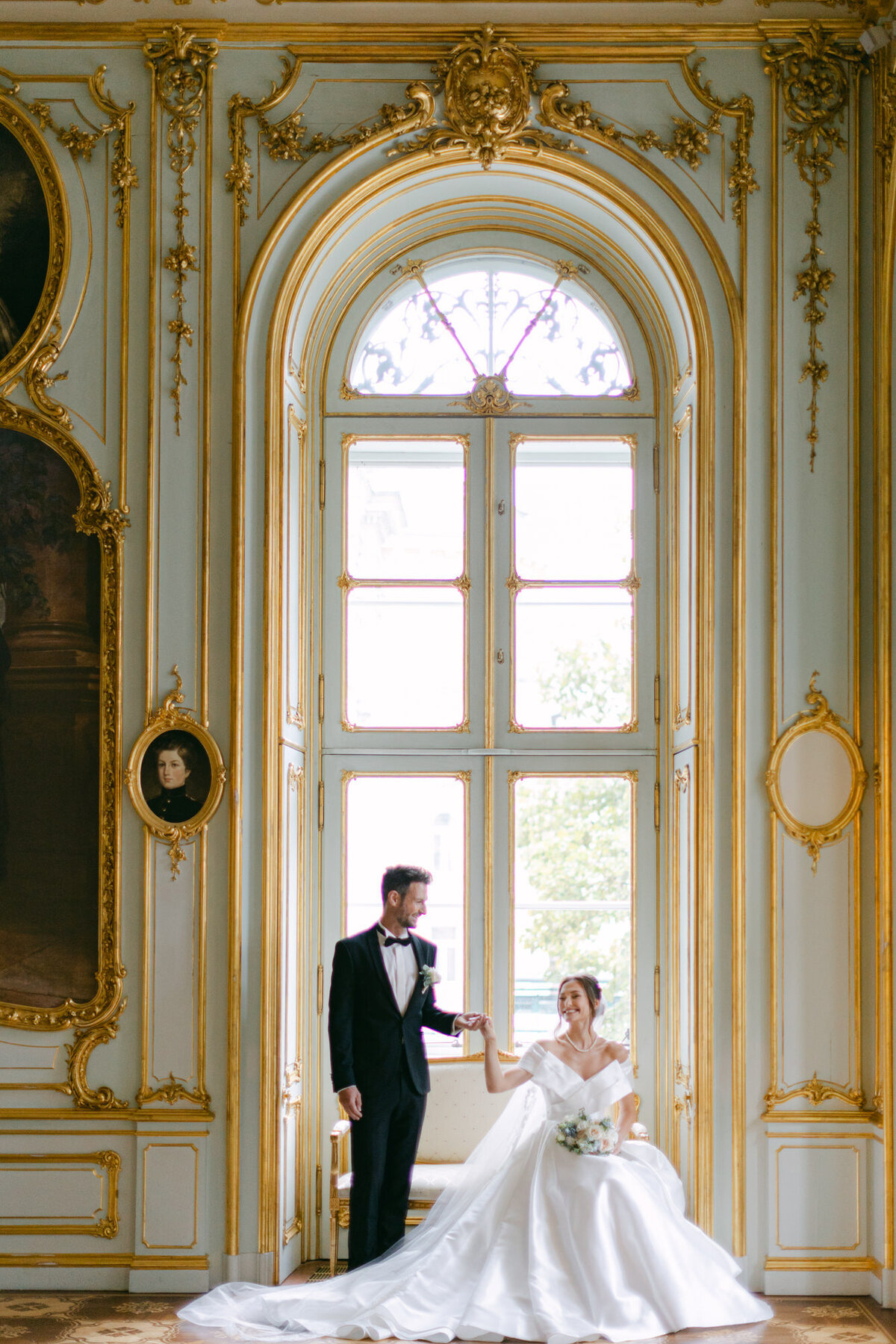Groom standing and looking at his beautiful bride sitting in the heritage room at luxury Villa Coburg