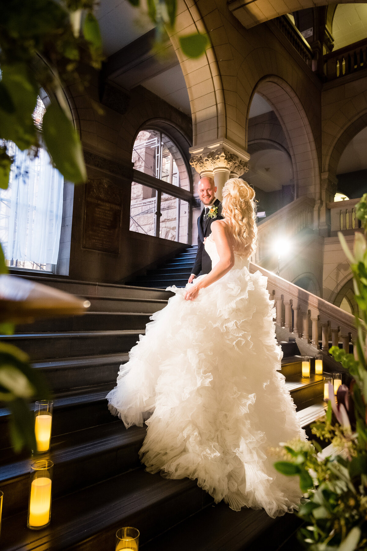 bride and groom walking up staircase at allegheny county courthouse with candles on sides and big fluffy wedding dress