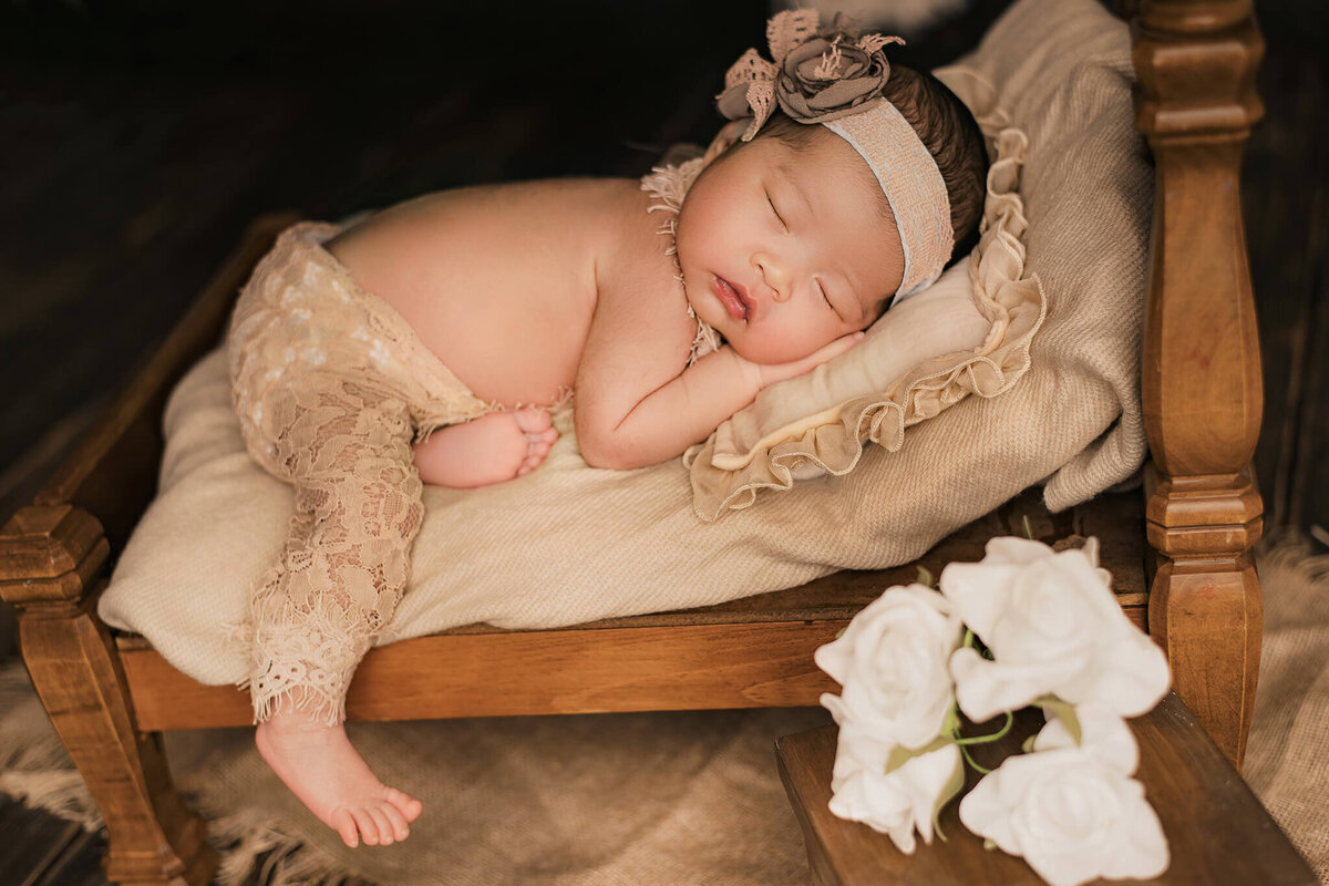 Infant girl sleeping on a newborn prop bed for her studio session.