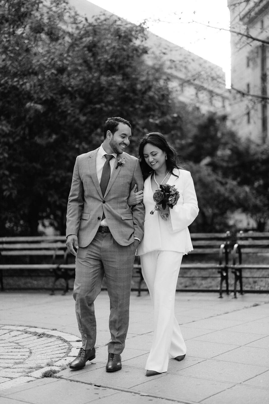 The bride and groom are happily walking in the park after eloping at New York City Hall. Image by Jenny Fu Studio