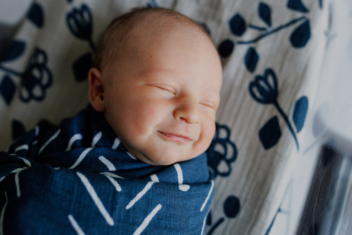 newborn smiling and laying in hospital bassinet with complimentary blue blankets