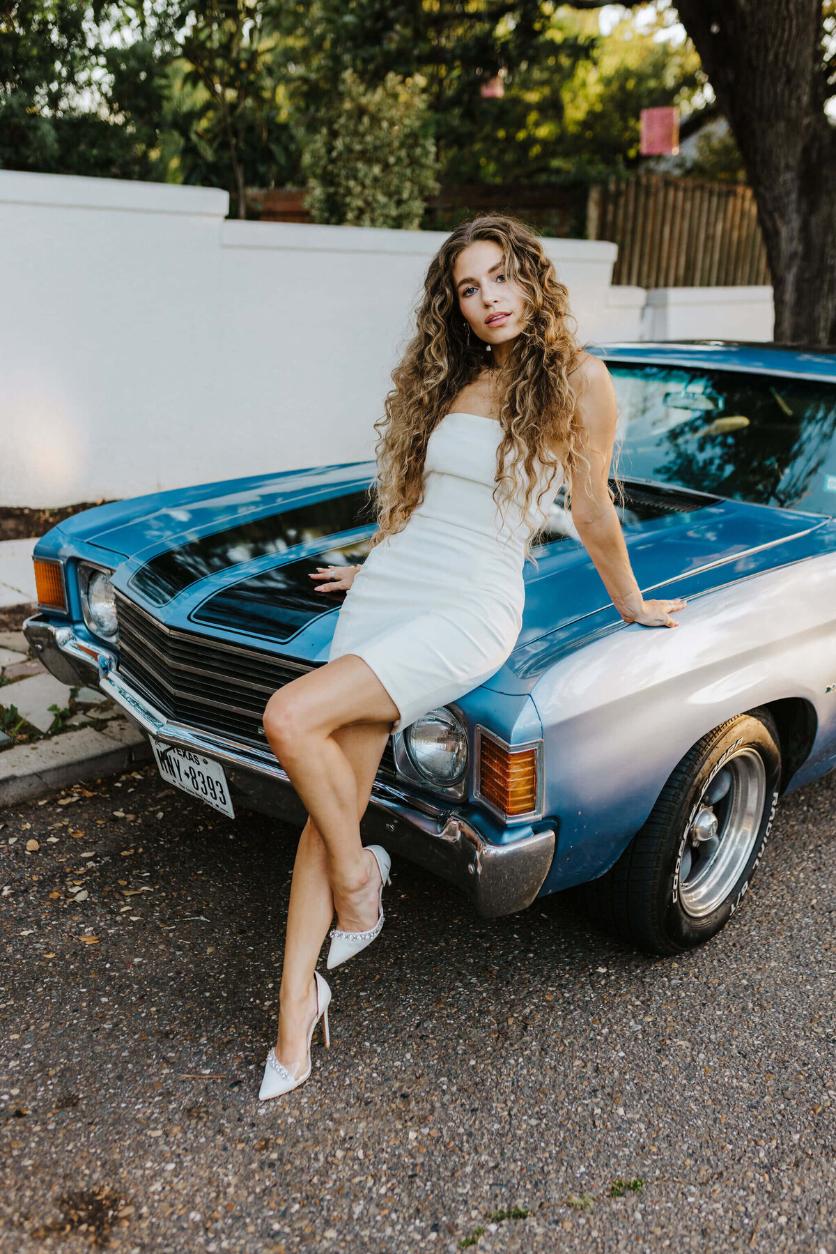 photo of bride in short white wedding gown leaning on vintage car at Tyler Texas wedding venue