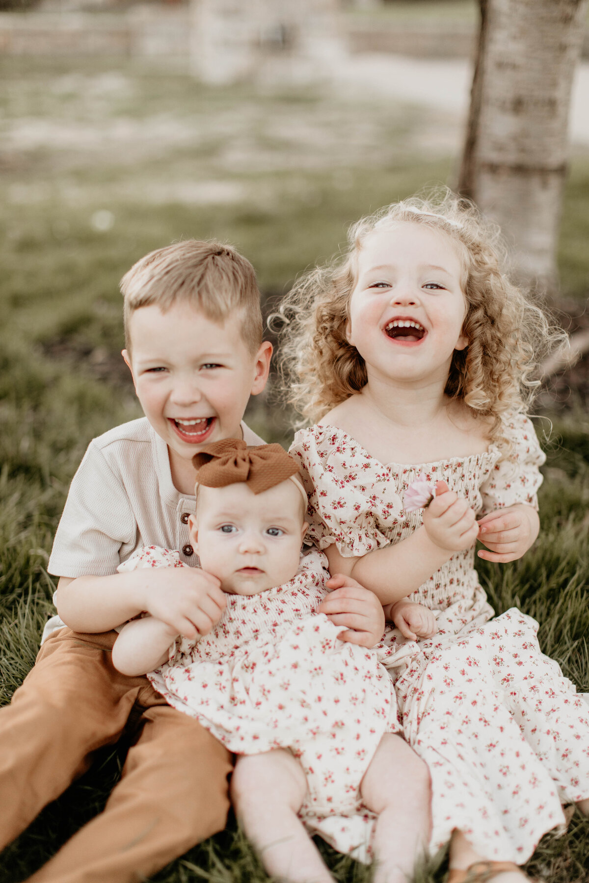 Three kids laughing and having fun while baby sister is in their laps.