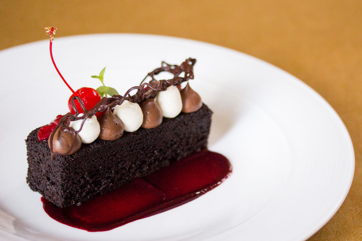 Chocolate cake served with hazelnut mousse, coffee meringue buttercream, espresso kahlúa ganache, strawberry sauce, and chocolate garnish.