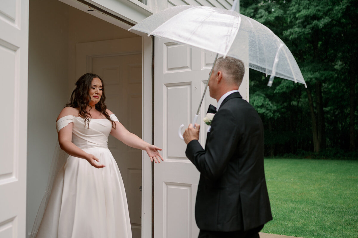 Bride smiling at her father before the ceremony as he shields her with an umbrella outside The Morris Estate.