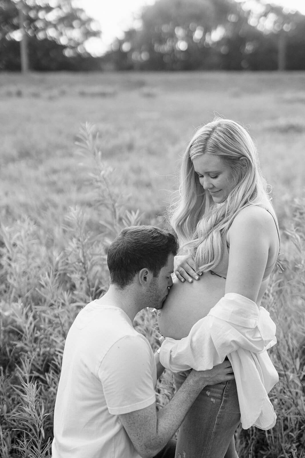 Man kissing baby bump standing in a field for  maternity session in Finger Lakes, New York