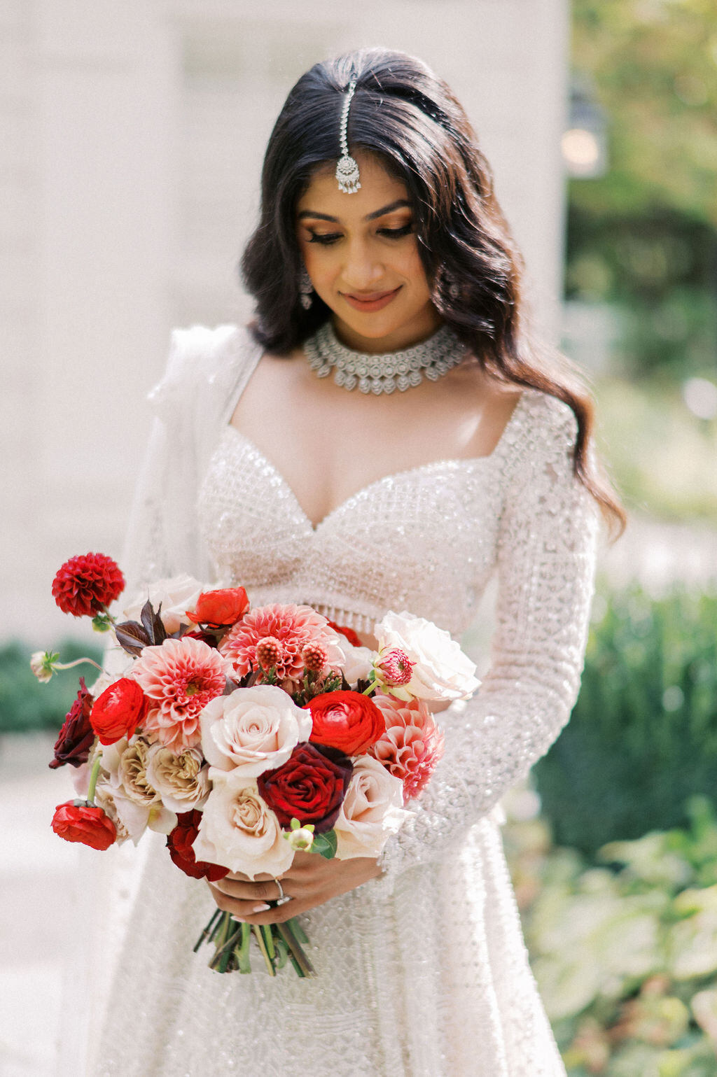 Bride in embellished gown holding a red and blush floral bouquet during portraits at Old Edwards Inn in Highlands, NC.