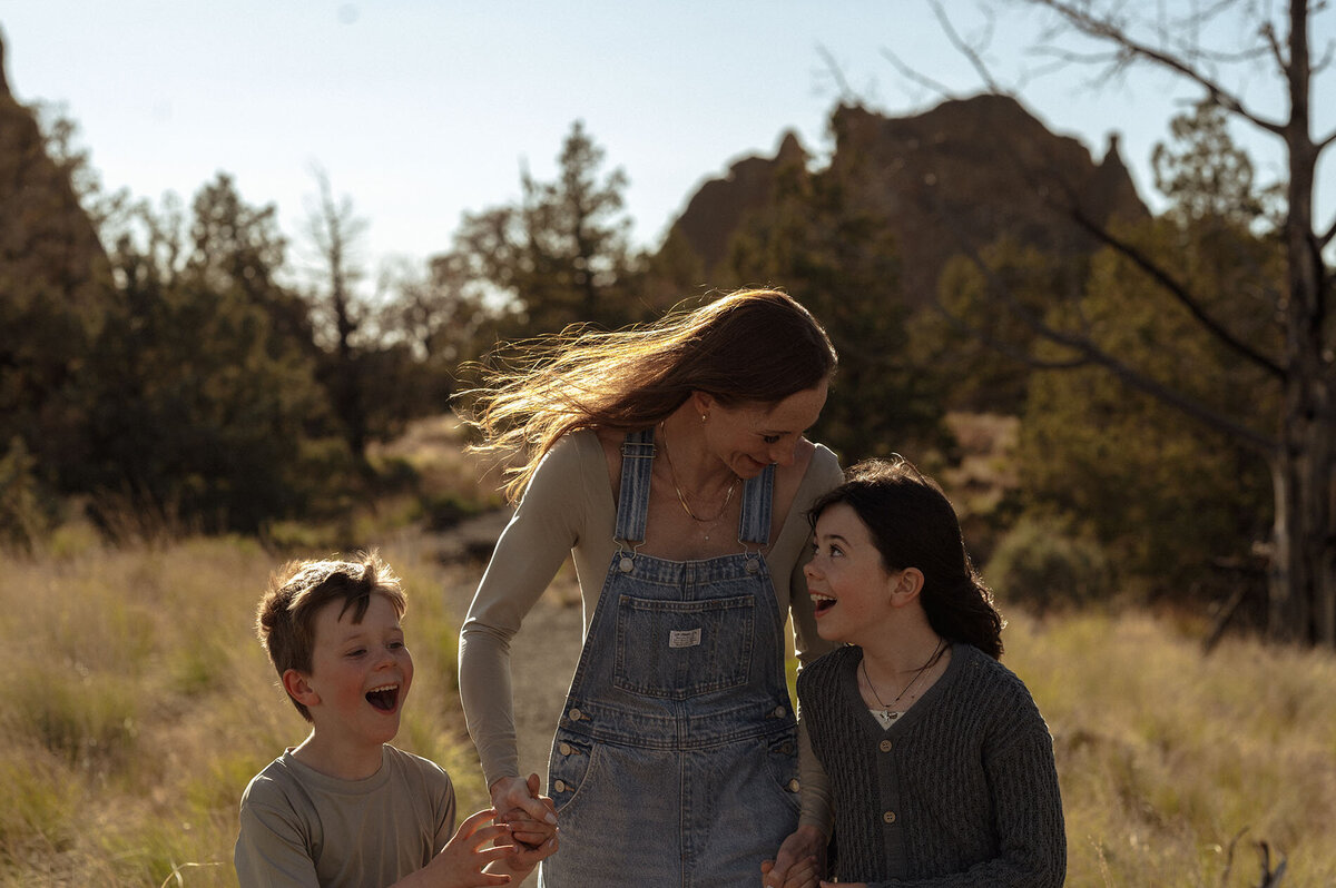 playful family photo of woman and children laughing and running through the rugged landscape of Smith Rock