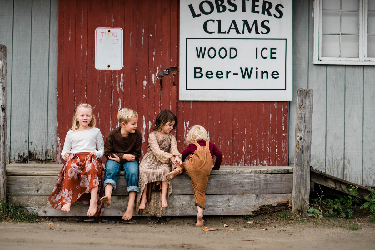 Children helping each other onto ledge outdoor family photography Maine