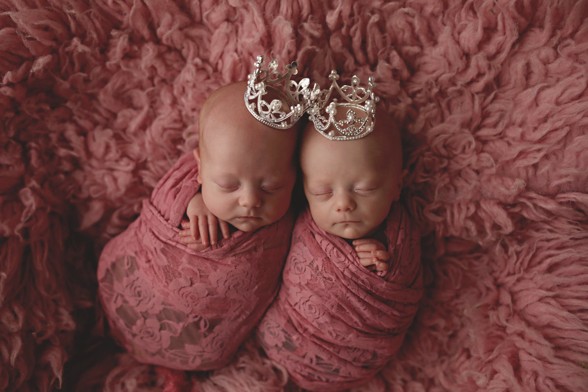newborn twins wrapped in rose pink lace posed on pink fur blanket
