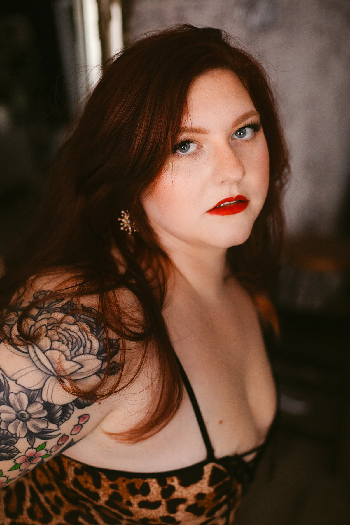 A woman in a cheetah print top with red hair and red lipstick looks seductively at the camera at a Bentonville boudoir photoshoot.